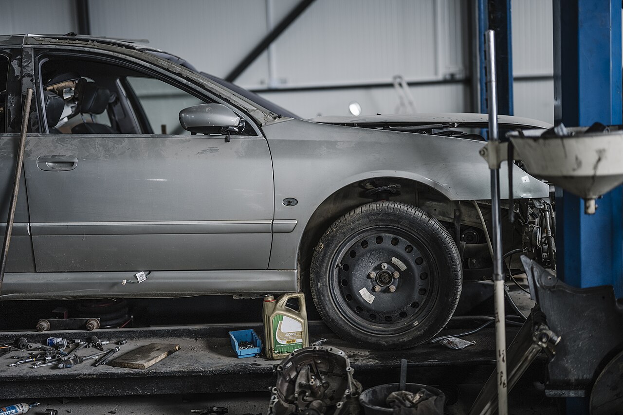 Een auto op de hefbrug in een werkplaats, met gereedschap en onderdelen op de vloer